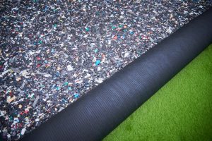 Close-up view of an underlay roll for carpet tiles, made of rubber. Green carpet tile sample displayed beside it.