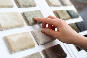 A hand touches a sample of a carpet tile on a display board featuring various shades of carpet tile samples, showcasing different carpet tile design ideas.