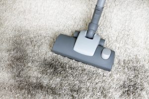 Vacuum cleaning dirt off exterior carpet tiles, demonstrating the importance of regular maintenance for outdoor carpet longevity and cleanliness.