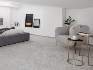 Bedroom with grey bed, grey chair, and decor, showing carpet fading due to sunlight exposure.