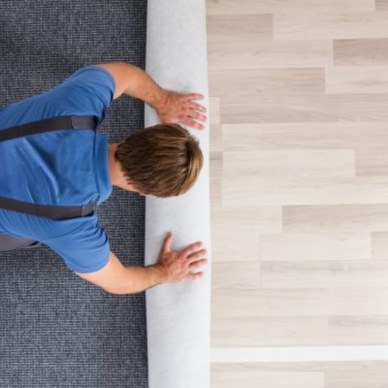 A man in blue rolls carpeted flooring in Campbelltown, surrounded by a cosy indoor setting.